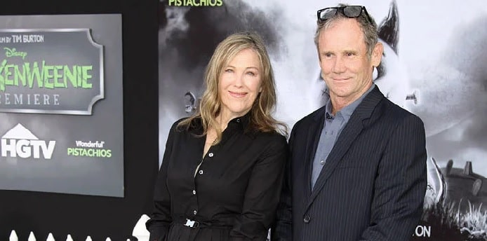 Catherine O'Hara in black dress with her husband smiling who is in blue shirt black coat